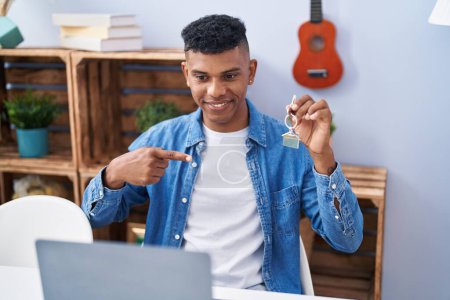 Téléchargez les photos : Jeune homme hispanique tenant les clés de la nouvelle maison faire appel vidéo sourire heureux pointant avec la main et le doigt - en image libre de droit
