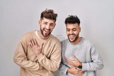 Téléchargez les photos : Jeune couple homosexuel debout sur fond blanc souriant et riant fort à haute voix parce que drôle blague folle avec les mains sur le corps. - en image libre de droit