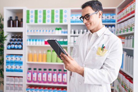 Photo for Young hispanic man pharmacist using touchpad working at pharmacy - Royalty Free Image