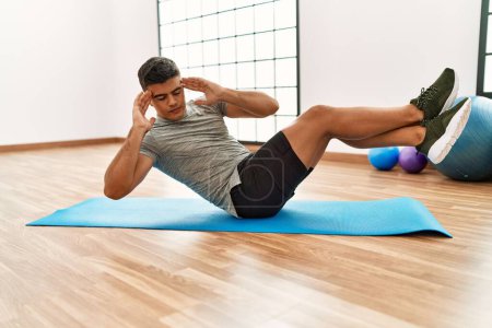 Photo for Young hispanic man training abs exercise at sport center - Royalty Free Image