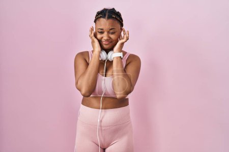Photo for African american woman with braids wearing sportswear and headphones covering ears with fingers with annoyed expression for the noise of loud music. deaf concept. - Royalty Free Image