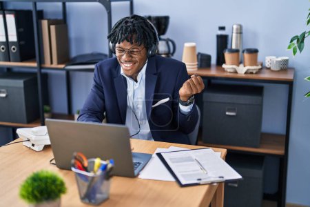 Téléchargez les photos : Young african man with dreadlocks working at the office wearing headset screaming proud, celebrating victory and success very excited with raised arm - en image libre de droit