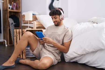 Foto de Young arab man listening to music sitting on floor at bedroom - Imagen libre de derechos