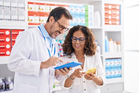 Man and woman pharmacists using touchpad and smartphone working at pharmacy