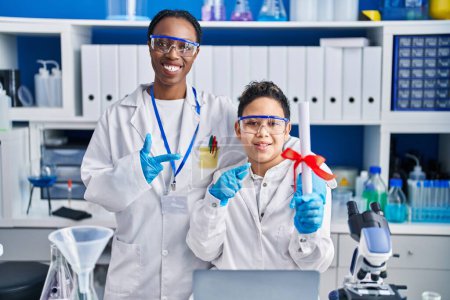 Mother and son at scientist laboratory smiling happy pointing with hand and finger 