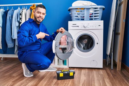 Foto de Hispanic repairman working on washing machine smiling happy pointing with hand and finger - Imagen libre de derechos