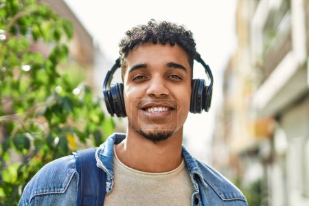 Téléchargez les photos : Jeune homme hispanique écoutant de la musique portant des écouteurs dans la rue - en image libre de droit