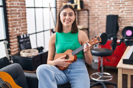 Photo for Young hispanic woman musician playing ukelele at music studio - Royalty Free Image