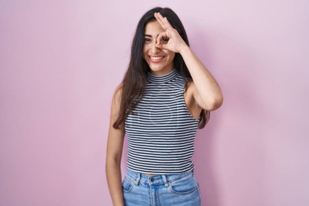 Foto de Young teenager girl wearing casual striped t shirt doing ok gesture with hand smiling, eye looking through fingers with happy face. - Imagen libre de derechos
