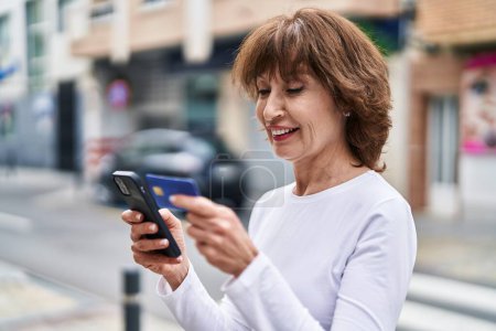 Photo for Middle age woman using smartphone and credit card at street - Royalty Free Image