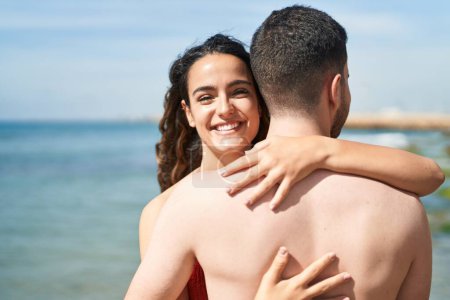 Photo for Young hispanic couple tourists wearing swimsuit hugging each other at seaside - Royalty Free Image