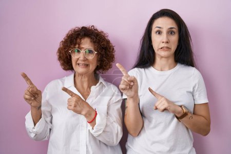 Photo for Hispanic mother and daughter wearing casual white t shirt over pink background pointing aside worried and nervous with both hands, concerned and surprised expression - Royalty Free Image