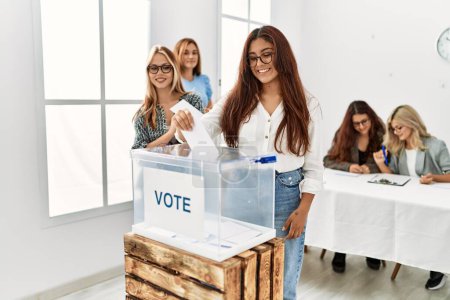 Téléchargez les photos : Groupe de jeunes électrices souriantes heureux de mettre le vote dans les urnes au centre électoral. - en image libre de droit