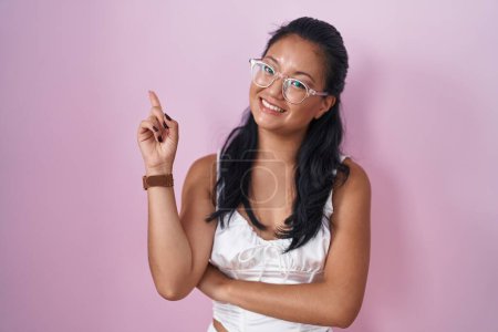 Photo for Asian young woman standing over pink background smiling happy pointing with hand and finger to the side - Royalty Free Image