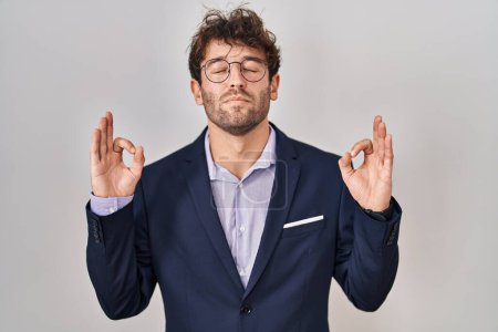 Téléchargez les photos : Homme d'affaires hispanique portant des lunettes se détendre et sourire les yeux fermés en faisant geste de méditation avec les doigts. concept de yoga. - en image libre de droit