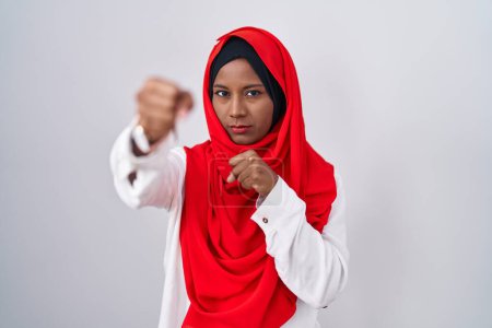 Photo for Young arab woman wearing traditional islamic hijab scarf punching fist to fight, aggressive and angry attack, threat and violence - Royalty Free Image