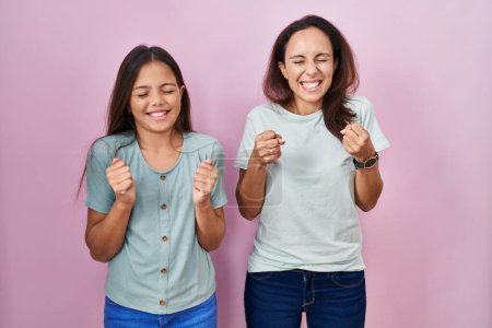 Téléchargez les photos : Young mother and daughter standing over pink background excited for success with arms raised and eyes closed celebrating victory smiling. winner concept. - en image libre de droit