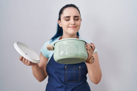 Photo for Young modern girl with blue hair wearing apron holding cooking pot winking looking at the camera with sexy expression, cheerful and happy face. - Royalty Free Image