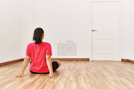Foto de Mujer hispana hermosa joven sentada en el piso en la vista trasera en la habitación vacía - Imagen libre de derechos