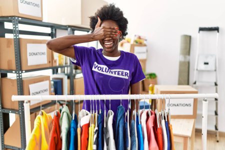 Téléchargez les photos : African young woman wearing volunteer t shirt at donations stand smiling and laughing with hand on face covering eyes for surprise. blind concept. - en image libre de droit