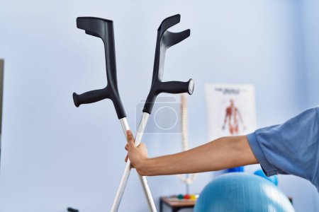 Photo for Young blond man pysiotherapist holding crutches at rehab clinic - Royalty Free Image