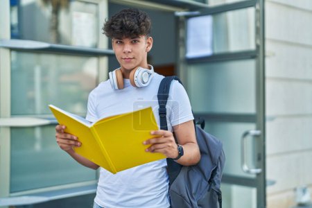 Foto de Joven estudiante adolescente hispano usando libro de lectura de mochila en la universidad - Imagen libre de derechos