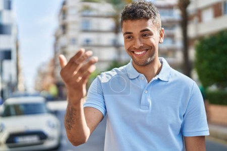 Téléchargez les photos : Afro-américain homme souriant confiant faire geste à venir avec le doigt dans la rue - en image libre de droit