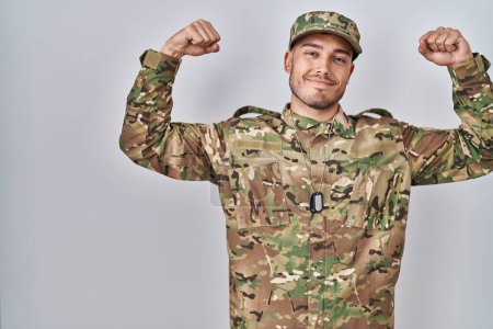 Photo for Young hispanic man wearing camouflage army uniform showing arms muscles smiling proud. fitness concept. - Royalty Free Image