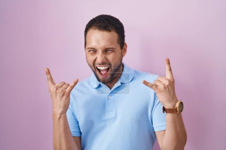 Photo for Hispanic man standing over pink background shouting with crazy expression doing rock symbol with hands up. music star. heavy music concept. - Royalty Free Image