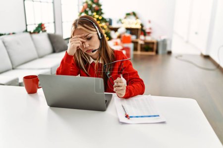 Téléchargez les photos : Jeune caucasienne agent du centre d'appels souligné télétravail assis par arbre de Noël à la maison - en image libre de droit