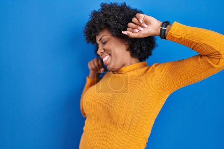 Photo for Black woman with curly hair standing over blue background stretching back, tired and relaxed, sleepy and yawning for early morning - Royalty Free Image
