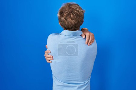 Téléchargez les photos : Caucasian man standing over blue background hugging oneself happy and positive from backwards. self love and self care - en image libre de droit