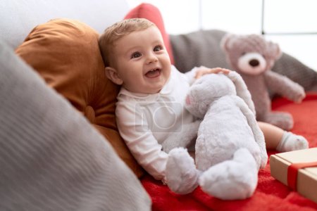 Photo for Adorable toddler holding teddy bear sitting on sofa at home - Royalty Free Image