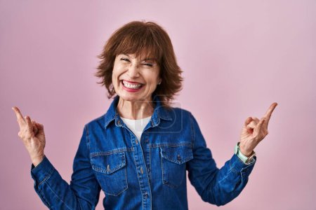 Photo for Middle age woman standing over pink background shouting with crazy expression doing rock symbol with hands up. music star. heavy music concept. - Royalty Free Image