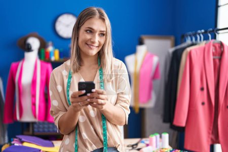 Photo for Young caucasian woman tailor smiling confident using smartphone at sewing studio - Royalty Free Image