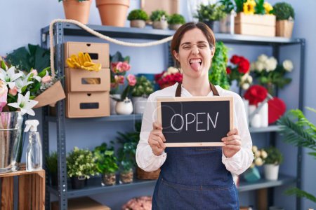 Photo for Brunette woman working at florist holding open sign sticking tongue out happy with funny expression. - Royalty Free Image