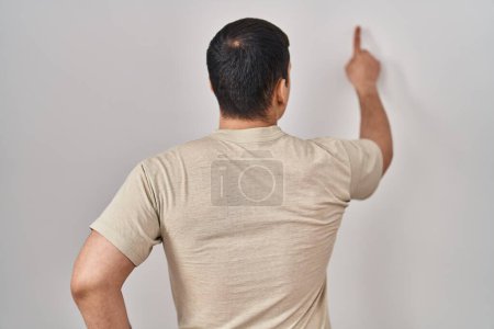 Foto de Hombre árabe joven con camiseta casual posando hacia atrás apuntando hacia adelante con la mano del dedo - Imagen libre de derechos