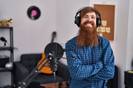 Téléchargez les photos : Jeune rousse homme musicien écouter de la musique assis avec les bras croisés geste au studio de musique - en image libre de droit