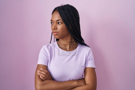 Téléchargez les photos : African american woman with braids standing over pink background looking to the side with arms crossed convinced and confident - en image libre de droit