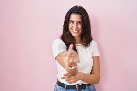 Téléchargez les photos : Young brunette woman standing over pink background beckoning come here gesture with hand inviting welcoming happy and smiling - en image libre de droit