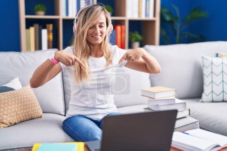 Foto de Mujer rubia joven estudiando el uso de ordenador portátil en casa buscando confiado con sonrisa en la cara, señalándose con los dedos orgullosos y felices. - Imagen libre de derechos
