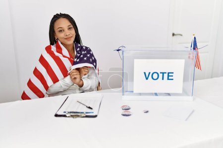 Téléchargez les photos : Jeune femme afro-américaine souriante et confiante portant le drapeau des États-Unis au collège électoral - en image libre de droit