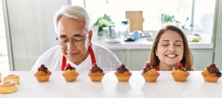 Photo for Middle age hispanic couple smiling happy smelling muffins at the kitchen. - Royalty Free Image