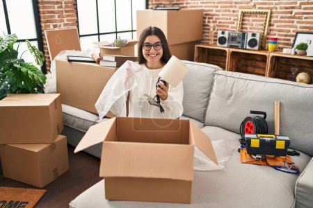 Photo for Young hispanic woman smiling confident unpacking cardboard box at new home - Royalty Free Image