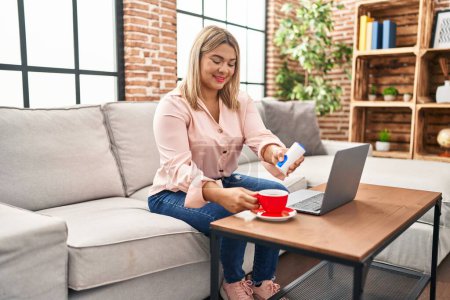 Photo for Young hispanic woman using laptop and drinking coffee sitting on sofa at home - Royalty Free Image