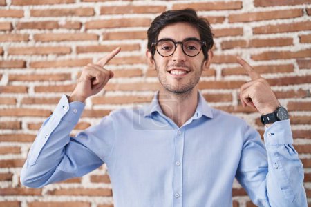 Photo for Young hispanic man standing over brick wall background smiling pointing to head with both hands finger, great idea or thought, good memory - Royalty Free Image