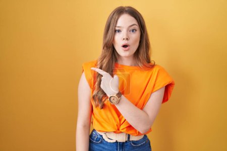 Téléchargez les photos : Caucasian woman standing over yellow background surprised pointing with finger to the side, open mouth amazed expression. - en image libre de droit