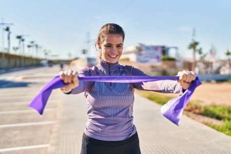 Photo for Young beautiful hispanic woman stretching arms using elastic band at street - Royalty Free Image