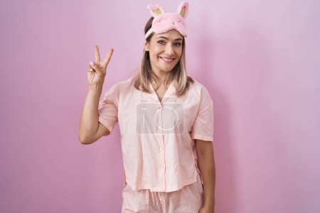 Téléchargez les photos : Blonde caucasian woman wearing sleep mask and pajama showing and pointing up with fingers number two while smiling confident and happy. - en image libre de droit