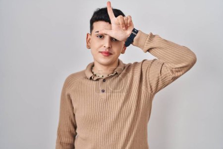 Téléchargez les photos : Non binary person standing over isolated background making fun of people with fingers on forehead doing loser gesture mocking and insulting. - en image libre de droit